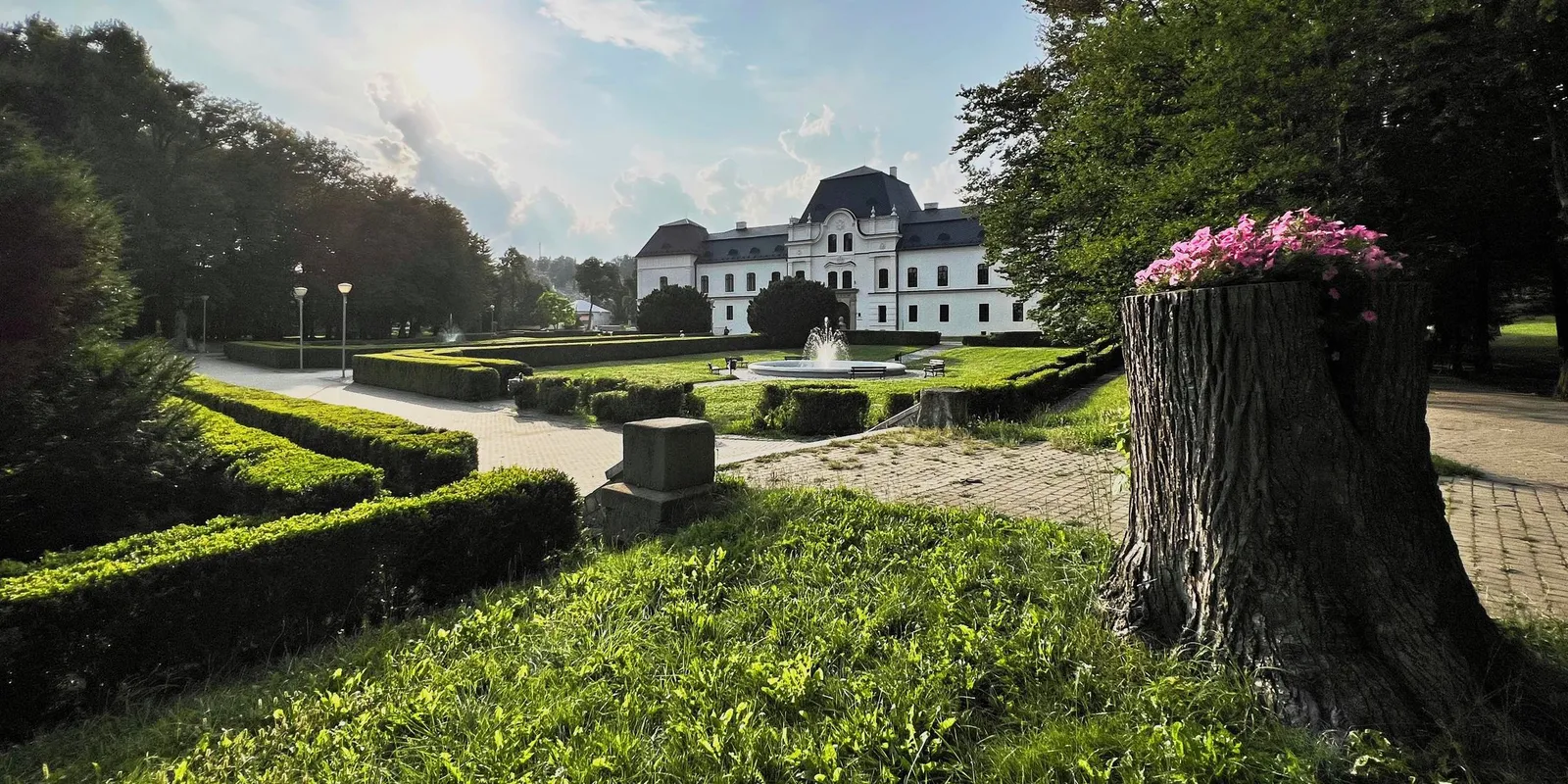 Zámocký park v Humennom s fontánou, strihanými živými plotmi a kaštieľom v pozadí