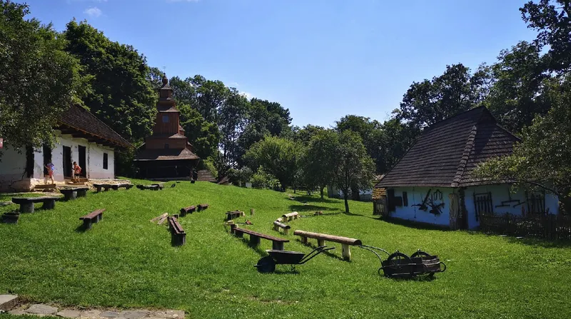 Drevené zrubové domy v skanzene v Humennom s kostolíkom v pozadí