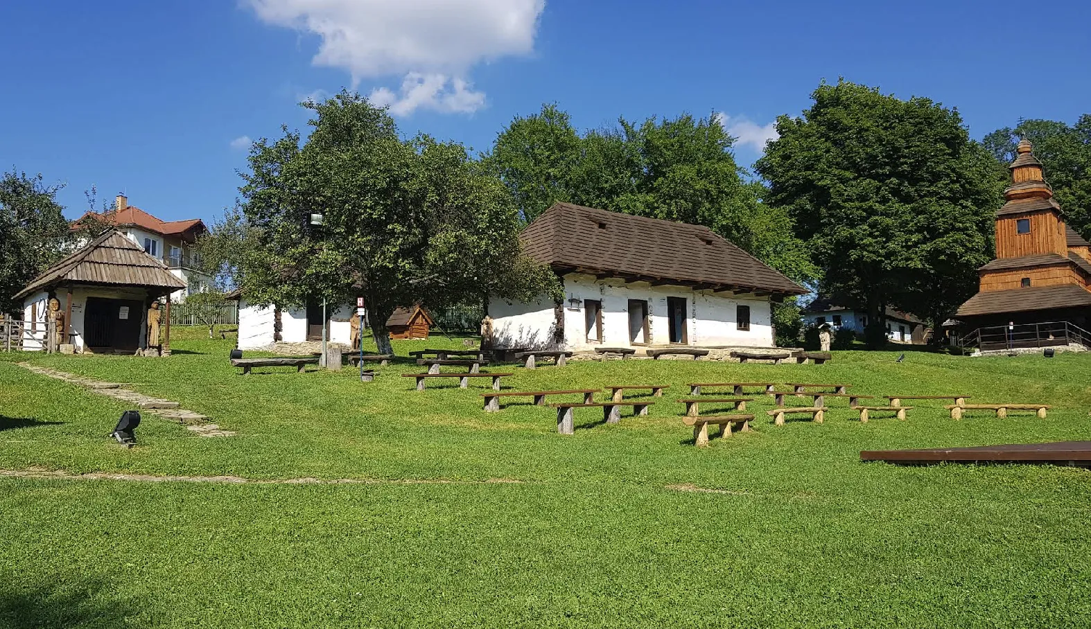 Drevené lavice medzi domami a drevený kostolík v skanzene v Humennom